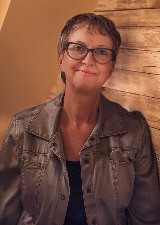 A portrait of Sue Pitchforth against a bright, wood background, by Seb Duper
