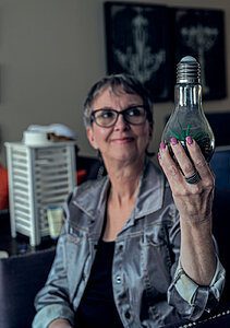 A portrait of Sue Pitchforth holding a decorated lightbulb, by Seb Duper