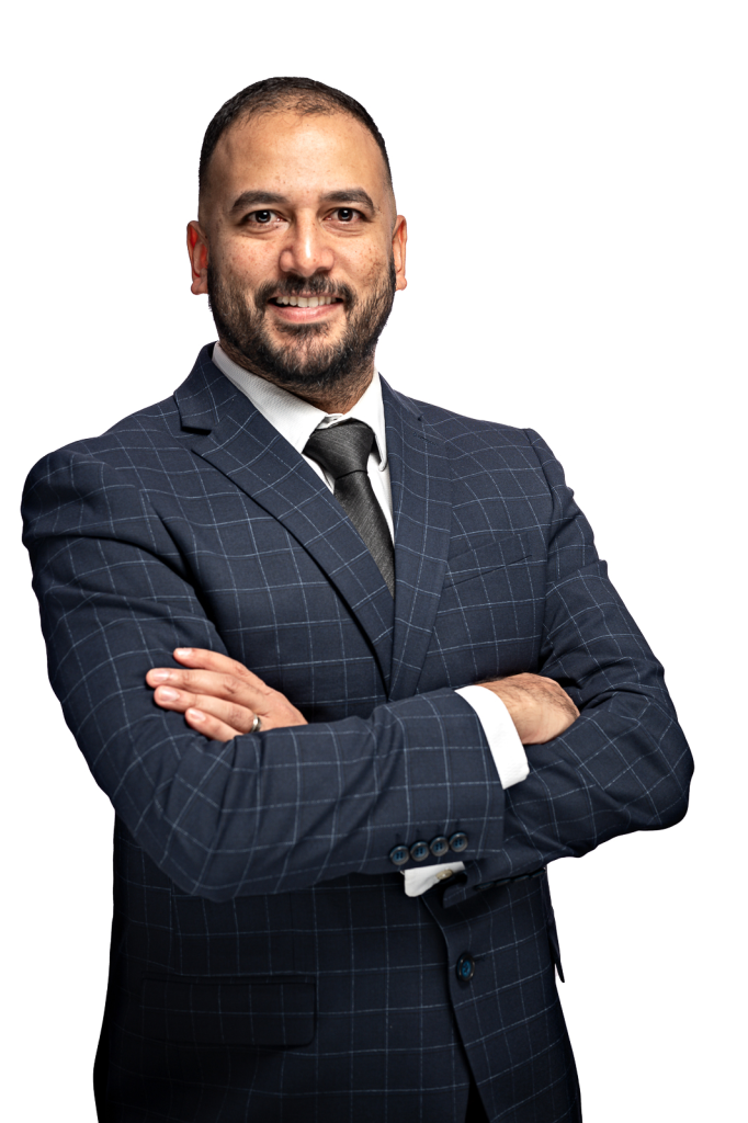 Professional headshot of a man wearing a dark blazer, with a white shirt and dark tie. His arms are crossed over his chest, and he is looking straight at the camera, smiling.