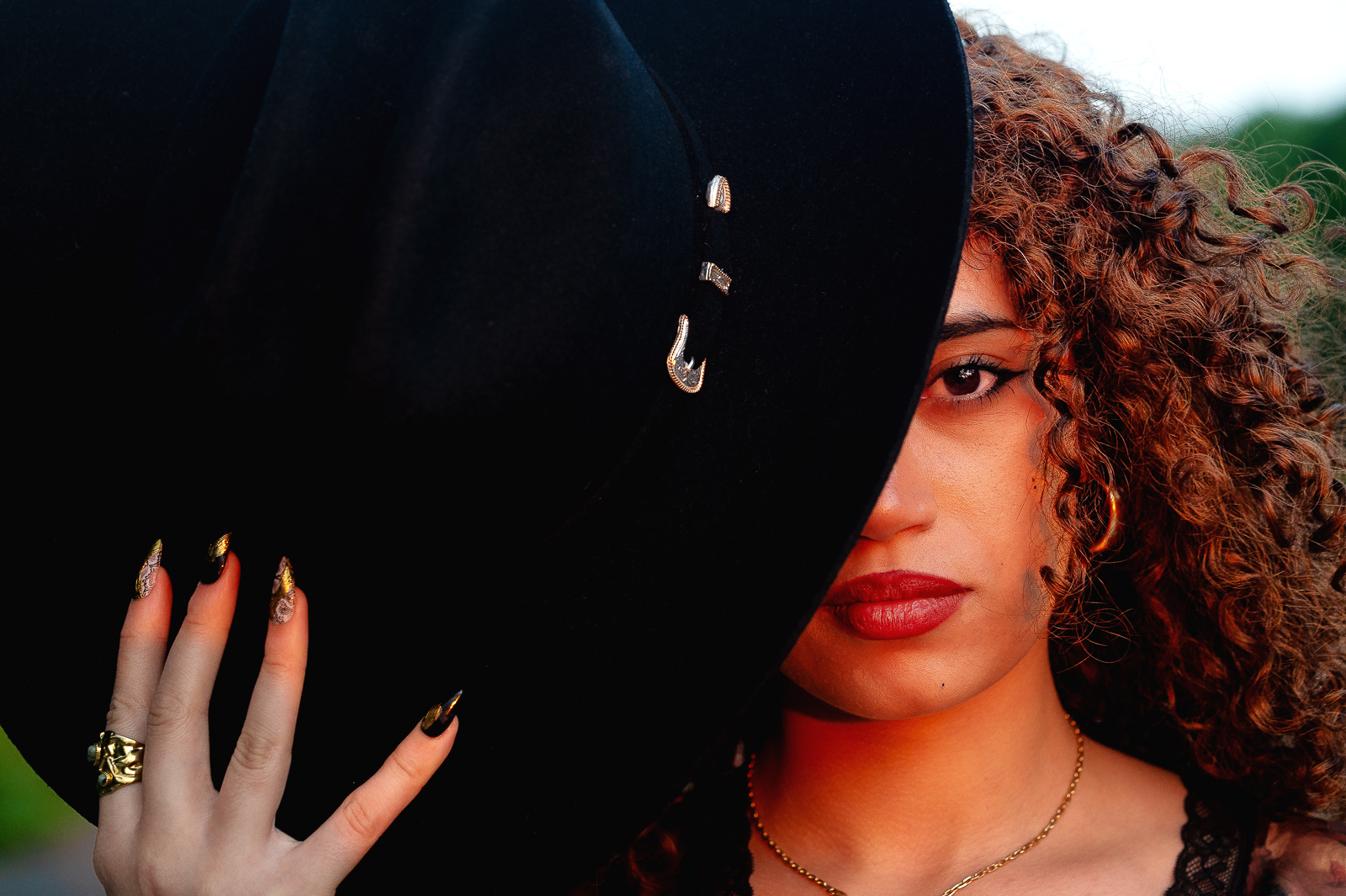 Close-up headshot of a young woman, the right half of her face is hidden by the black cowboy hat she's holding. Creative photography by Ottawa photographer Seb Duper.