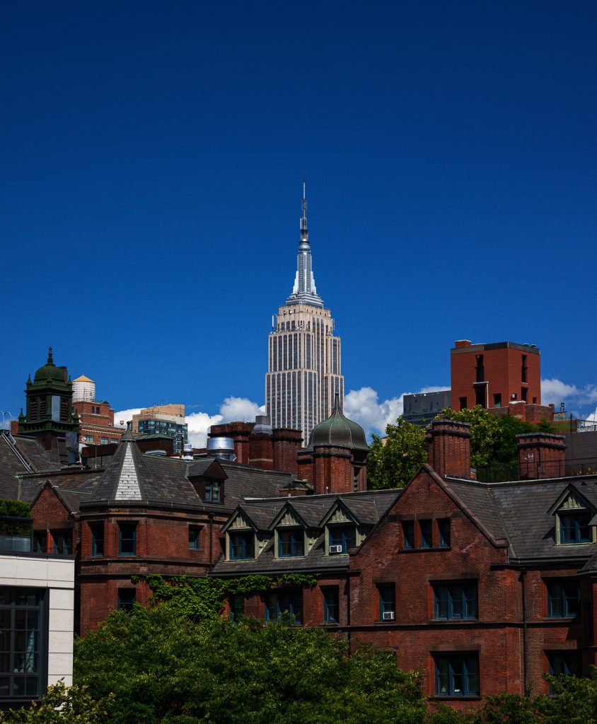 A Manhattan skyline, with brownstones in the foreground, and the Empire State building towering above them in the background.