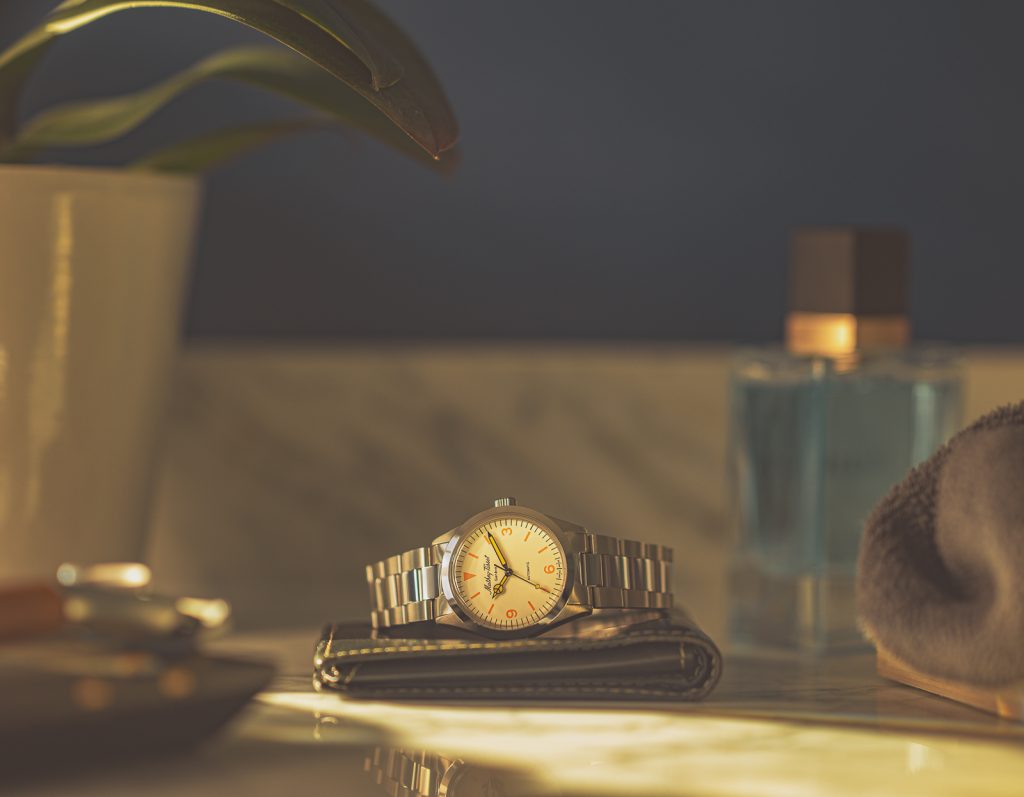 Lifestyle product photography featuring a men's wristwatch sitting on a wallet, on a marble counter. A bottle of cologne and a potted plant can be seen. Created by Ottawa professional freelance photographer Seb Duper