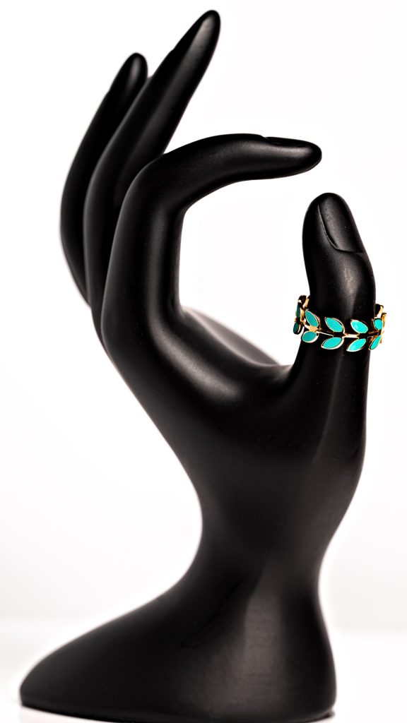 A plastic hand, painted black, with fingers curled. A small turquoise ring rests on the thumb. Product photography by Seb Duper.