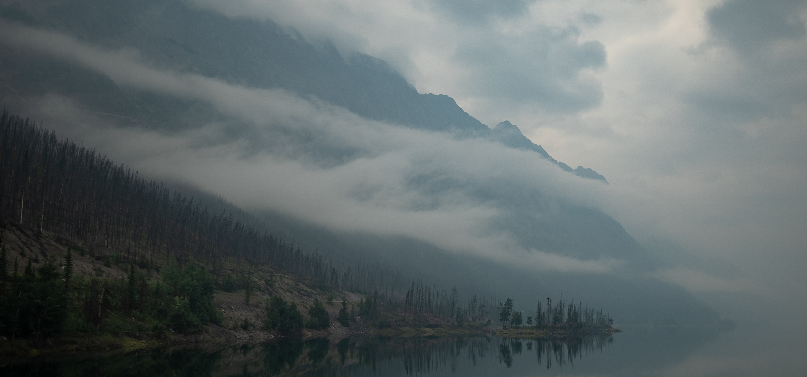 Fog and mist float above a lake, shrouding the mountains in the backdrop. Jasper, Alberta, Canada.