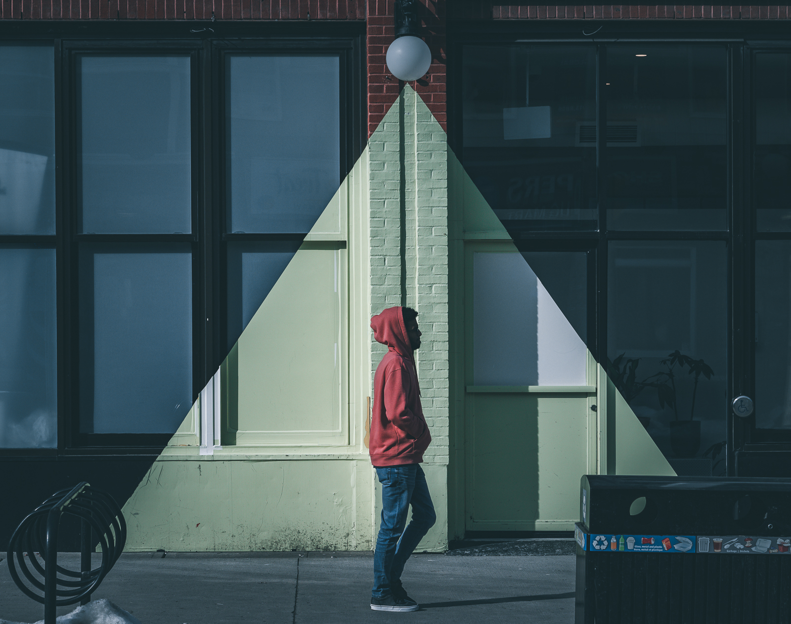 A man dressed in blue jeans and a red hoodie walking on a sidewalk in downtown Ottawa.