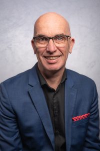 A headshot of an Ottawa entrepreneur, dressed in a black shirt with a dark blue sport jacket and a red pocket square.
