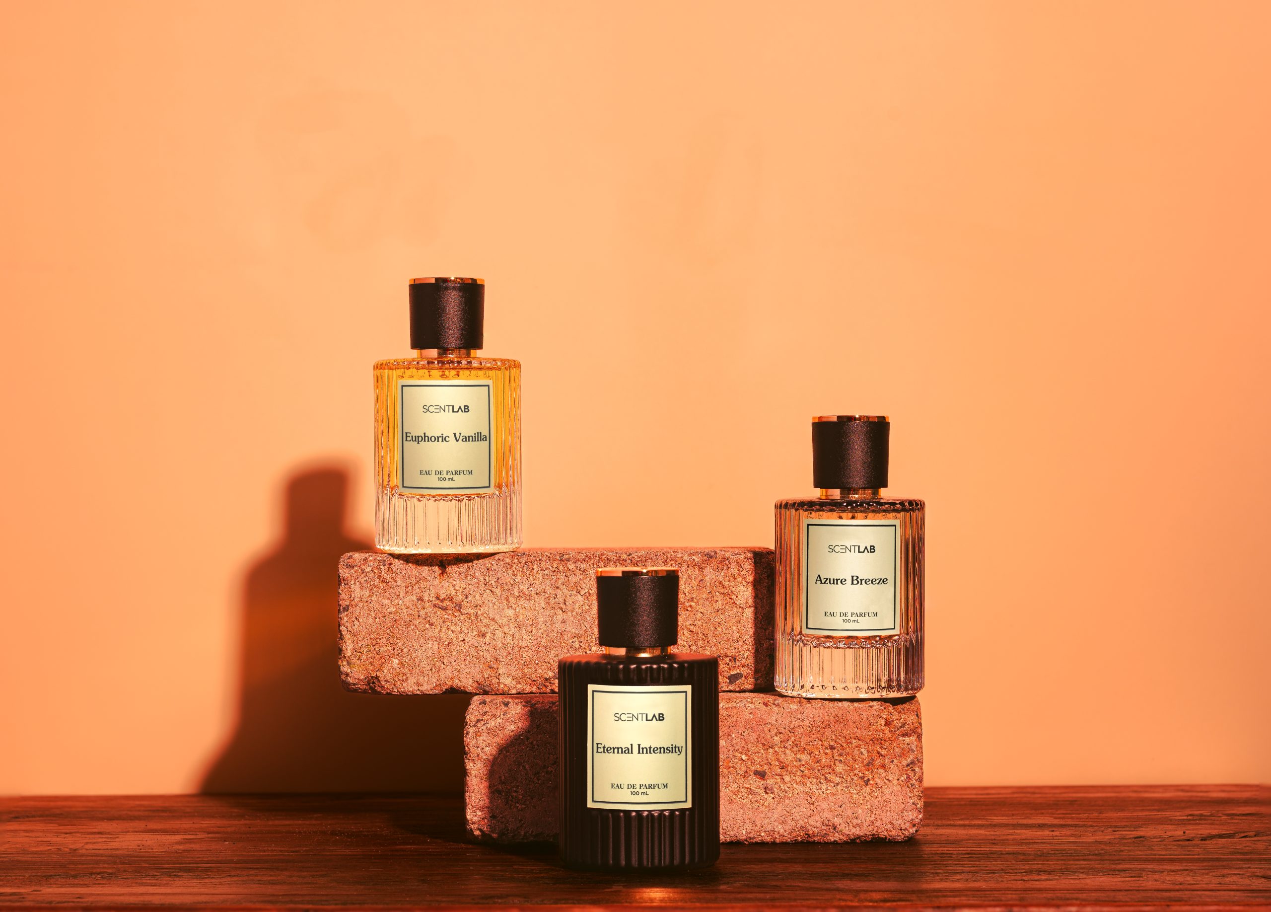 A bright photo of 3 men's perfume bottles, sitting on 2 stacked bricks, against a light orange coloured background.