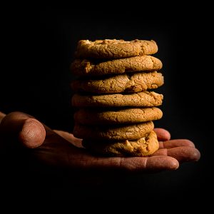 A pile of 7 chocolate chip cookies rests on an open hand, which seems to be floating against a black background.