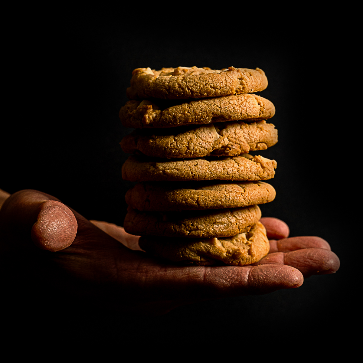 A pile of 7 chocolate chip cookies rests on an open hand, which seems to be floating against a black background.