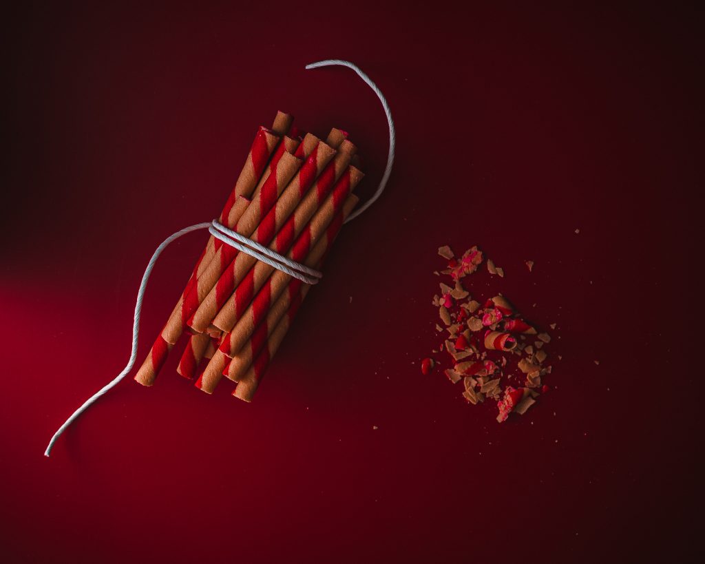 On the left, a bunch of red and white wafer rolls tied together with white cord, and wafer crumbs on the right. The background is dark red, and there's some light coming in from the bottom left.